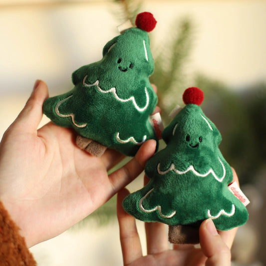 Two green plush Christmas trees with red berries held by a person against a blurred background.