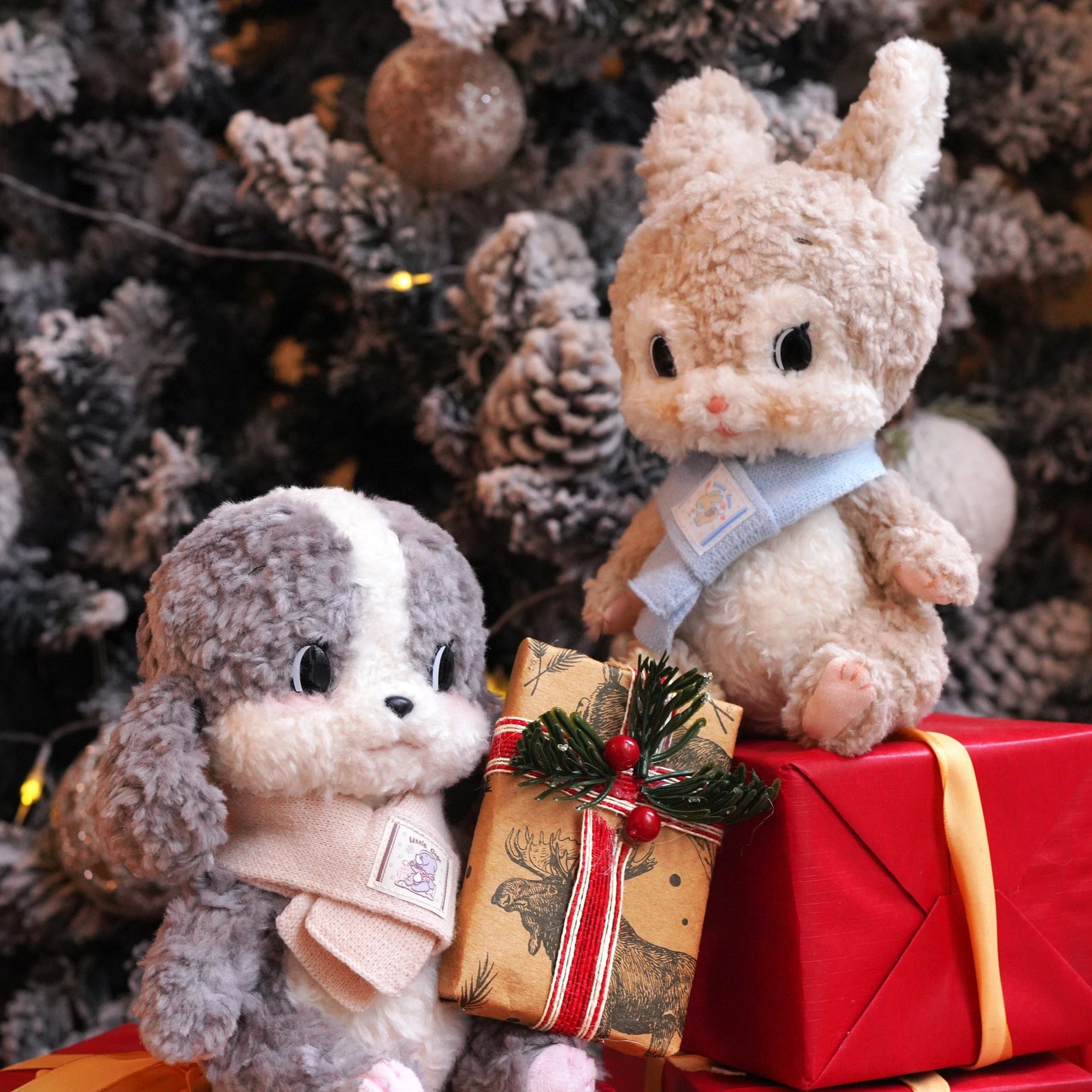 Two plush toys on red presents with a Christmas tree in the background