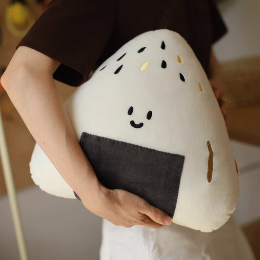 Person holding a plush rice ball toy with a smiley face design.