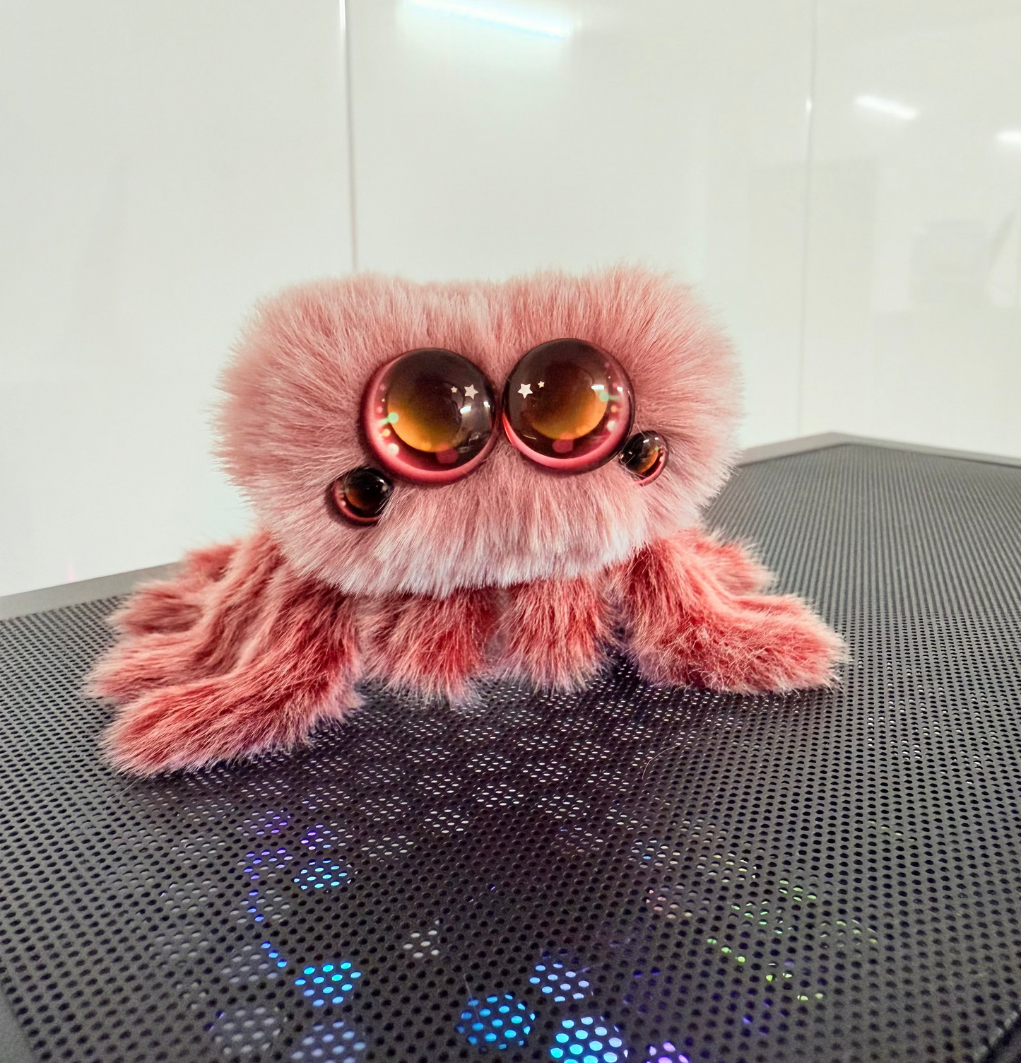 Pink plush toy with large eyes on a metallic surface
