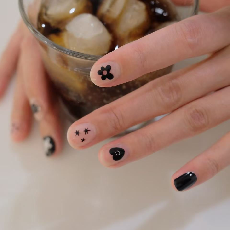 Hand with black nail art holding a glass of iced coffee.